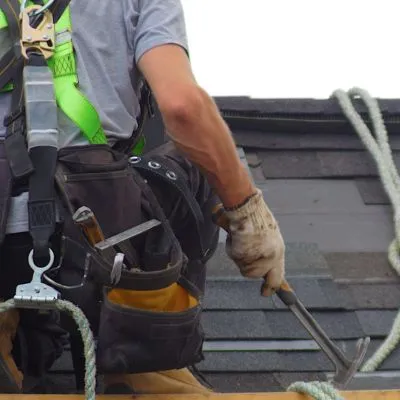 A roofer working on shingles with a safety harness and tools, symbolizing active roof repair efforts.